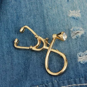 Detailed view of a gold-plated stethoscope brooch pinned to blue denim fabric