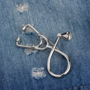 Polished silver stethoscope brooch with a sparkling diamond-cut crystal on denim background
