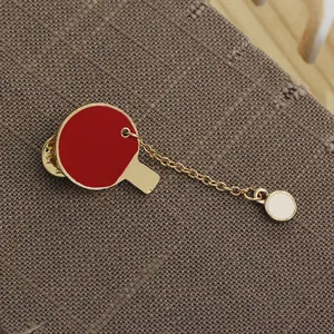 Detailed macro view of ping pong paddle brooch with red enamel and dangling white ball