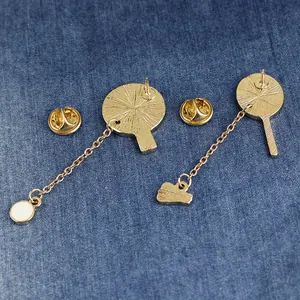 Golden badminton sports brooch pair with chain pendants on blue denim background