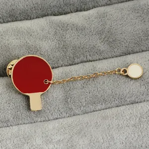 Detail of a gold ping pong paddle brooch with red enamel and chain link ball