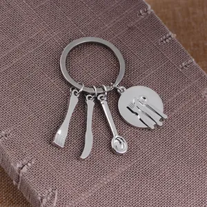 Polished silver keychain with kitchen cutlery pendants on dark textured fabric background