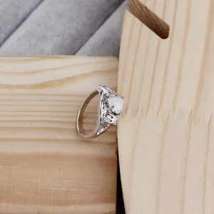 Close-up of heart-shaped white opal ring with silver hollow band on wooden stand