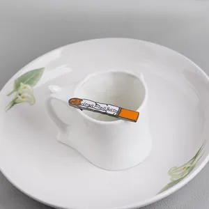 Creative enamel cigarette brooch with 'NEVER KNOWS BEST' text on white ceramic cup