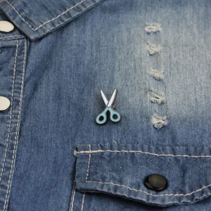 Detail of a cute blue and white enamel scissor brooch pinned to a denim shirt pocket
