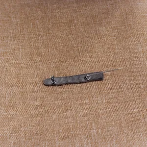 Detailed back view of a metal pin with secure clasp on textured fabric background