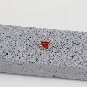 Detailed view of a cute watermelon slice enamel pin on a textured stone display