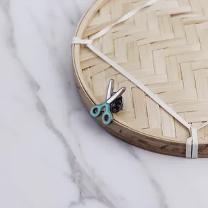 Cute cartoon scissor enamel pin with mint green handle on a woven bamboo background
