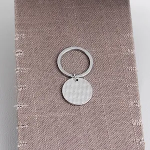 Détail macro du porte-clés rond en alliage avec surface texturée sur fond de toile de jute