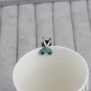Cute mint green enamel scissor brooch pin on a white ceramic cup edge for accessories