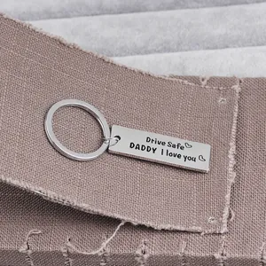 Close-up of Drive Safe DADDY engraved stainless steel keychain on a rustic fabric background