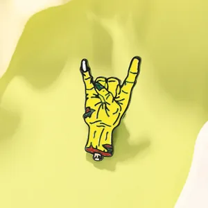 Close-up of a yellow zombie rock hand enamel pin on a minimalist green surface