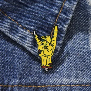 Detail of yellow zombie hand enamel pin featuring rock sign gesture on denim jacket