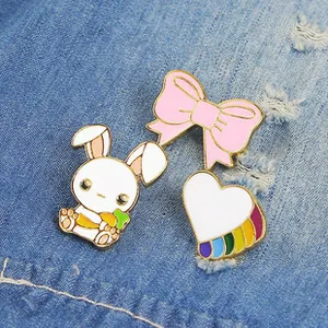 Close-up of three enamel pins including a rabbit, bow, and heart on blue denim fabric