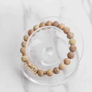 Detail of beaded natural stone bracelet with a gold metal bar engraved with Powerful text