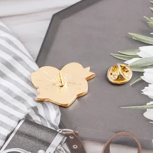 Macro shot of gold heart enamel pin back with butterfly clutch on a grey tray