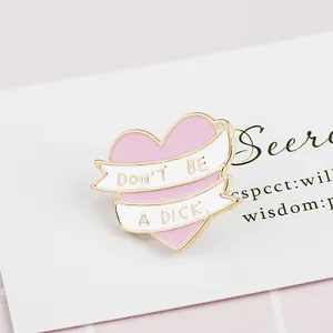 Pink heart enamel pin with gold edges featuring the phrase Don't Be a Dick on a white ribbon