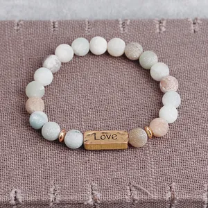 Detail of beaded bracelet with matte natural stones and gold Love engraved metal plate