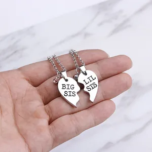 Detailed view of silver Big Sis and Lil Sis heart puzzle pendants held in hand