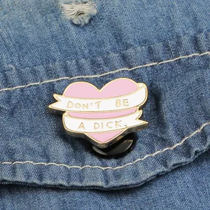 Pink heart enamel pin with gold Don't Be a Dick lettering on blue denim jacket