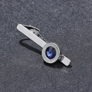 Polished silver tie clip with deep blue round crystal detail on a dark grey fabric background