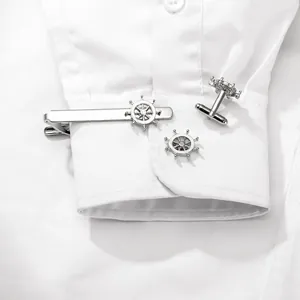 Polished silver tie clip and cufflinks set with nautical ship wheel design on a white shirt