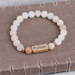 Macro detail of matte beaded bracelet with vintage bronze plaque engraved Forever