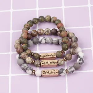 Detail of three-piece beaded stone bracelets with metallic plate engraved Confidence