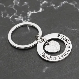 Detail of silver heart keychain engraved with Inspire, Learn, and Teach on stone background