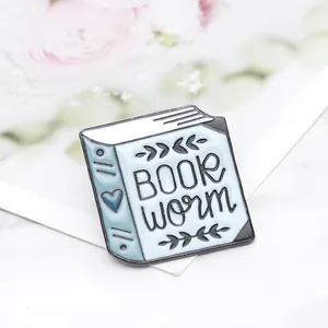 Dettaglio della spilla in smalto azzurro a forma di libro con decoro a cuore e foglie