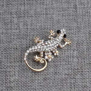 Elegante spilla a forma di geco in oro con strass di cristallo bianco su tessuto grigio