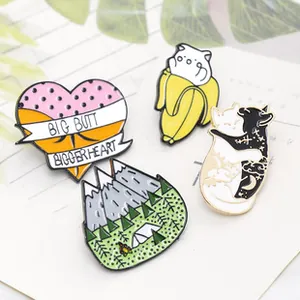 Close-up of four cute enamel pins featuring cats and fruit on a white paper card