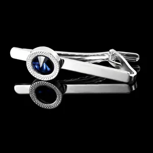 Close-up of silver tie clip with blue crystal and textured engraving on dark background
