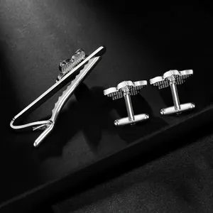 Macro shot of silver floral cufflinks and tie clip set on a black textured surface