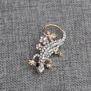 Dettaglio spilla a forma di lucertola dorata con strass scintillanti su tessuto grigio