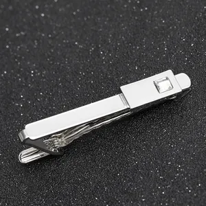 Close-up of polished silver tie clip with square-cut crystal on a dark textured background