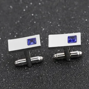 Close-up of rectangular silver cufflinks with blue gemstone on black glitter background