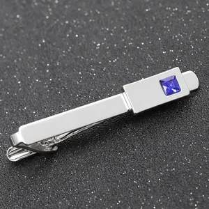 Macro view of silver tie clip featuring a square blue gemstone inlay on black texture