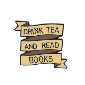 Cremefarbener Emaille-Anstecker in Schleifenform mit dem Spruch Drink Tea and Read Books
