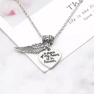 Close-up of angel wing and heart pendant with engraved memorial text on a silver necklace
