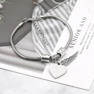 Macro detail of heart and feather wings charms on adjustable silver snake chain bracelet