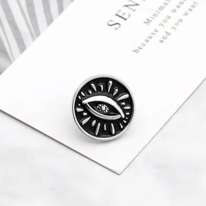 Gothic black evil eye enamel pin with silver eyelashes on minimalist card background