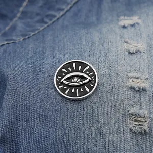 Close-up of a punk-style black evil eye enamel pin badge pinned on blue denim fabric