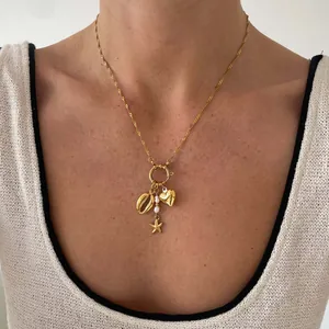 Detailweergave van een vergulde paperclipketting met schelp- en sterhangers aan de nek