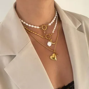 Detail van gelaagde 18k vergulde kettingen met barokparels en een hartvormige hanger