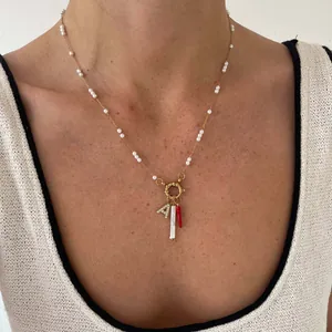 Detail van paperclip ketting met parel, rode hanger en letter A bezet met kleine diamanten