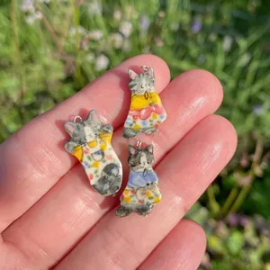 Detailed view of hand-painted ceramic cat pendants with colorful patterns held in hand