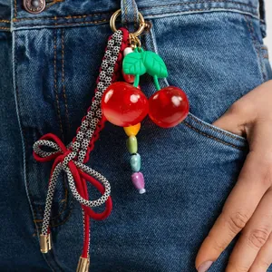 Detail of vibrant red cherry pendant with colorful beads and woven bow on denim fabric