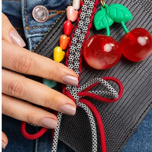 Colorful cherry and heart bead bag charm with a black and white bow on a black handbag