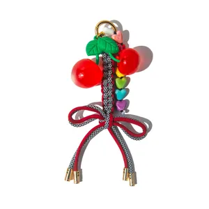 Colorful cherry keychain with heart beads and woven bow on a white background